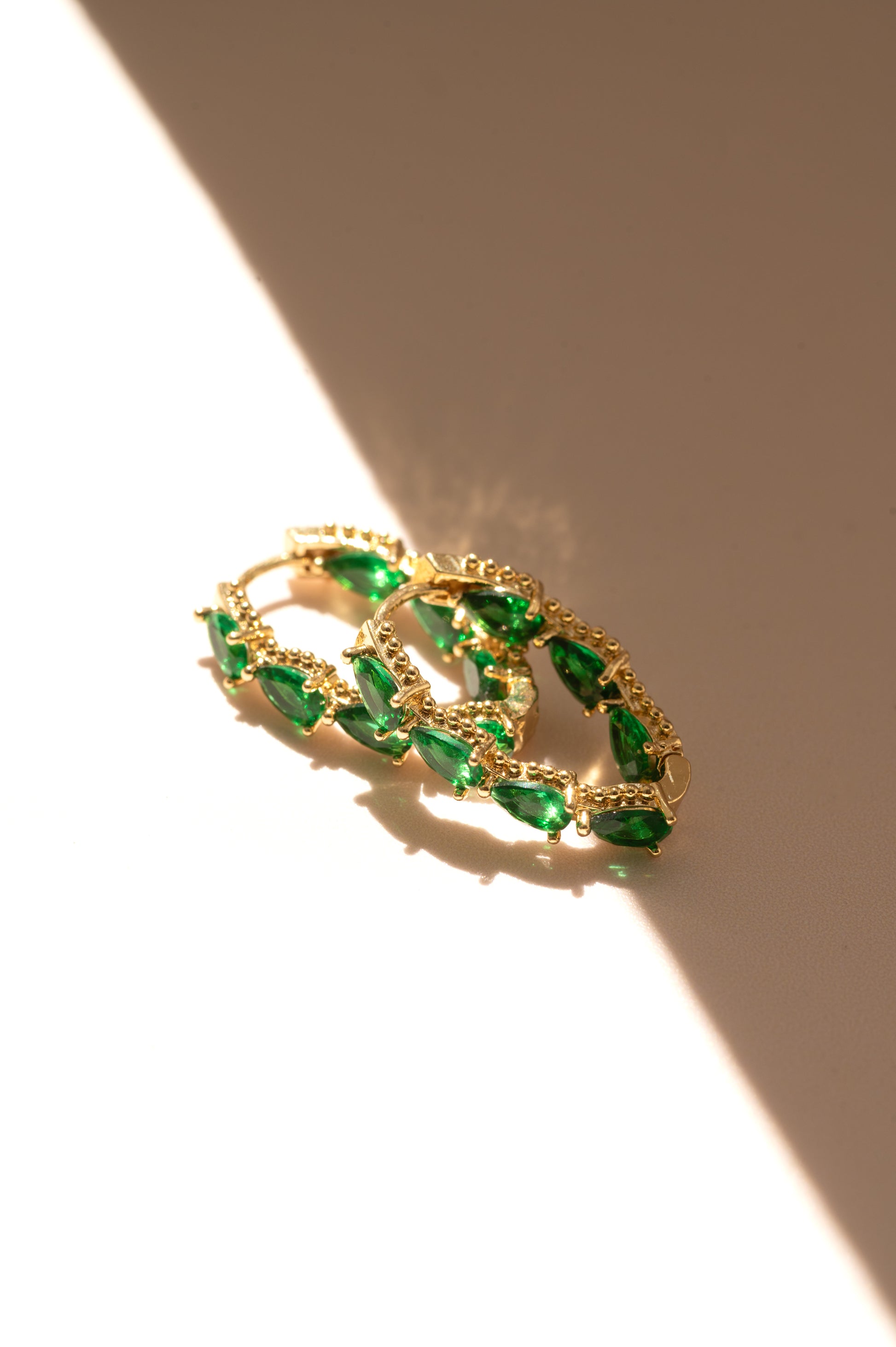 Gold hoops with emerald gemstones on a beige background