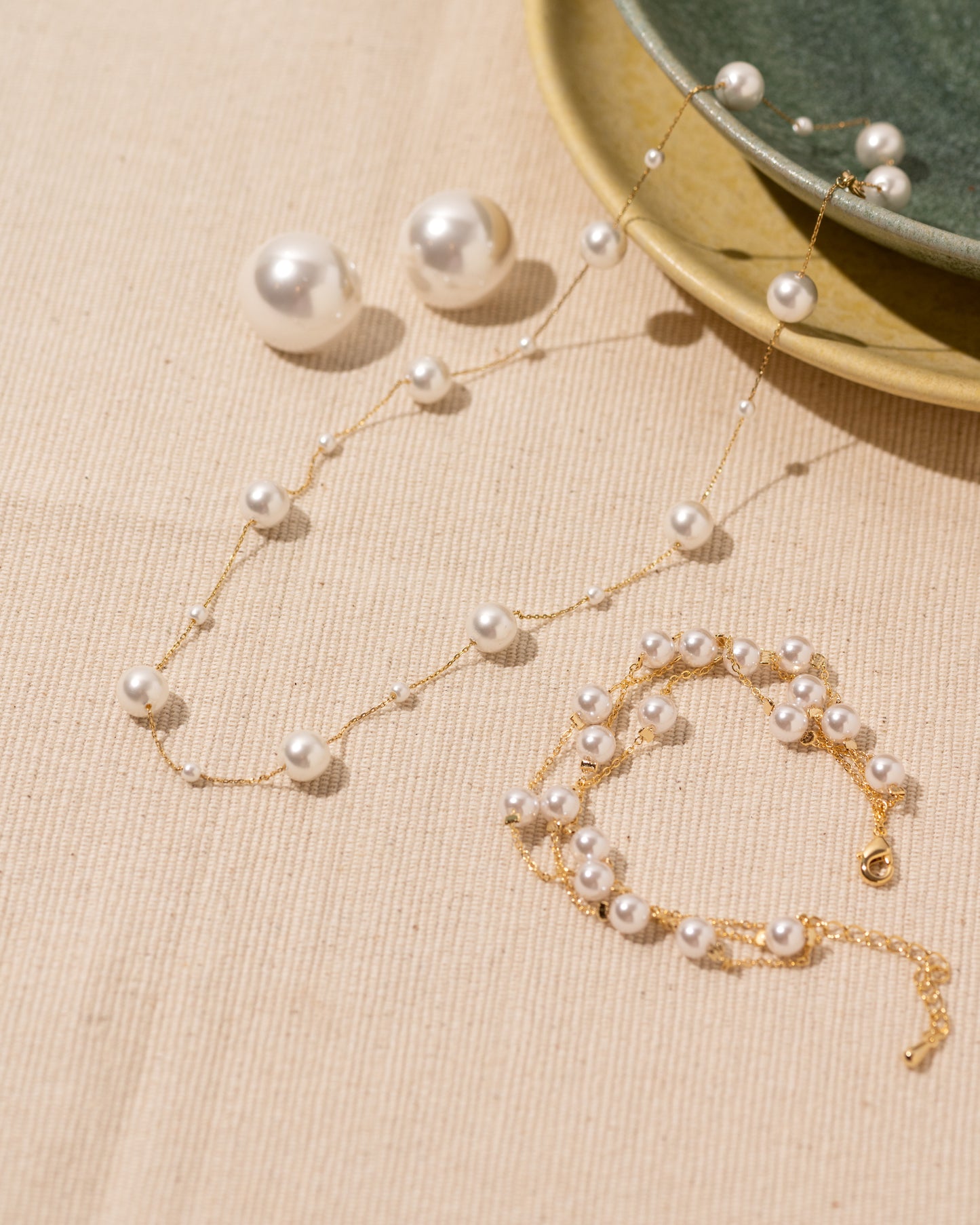 Pearl necklace and bracelet set on a beige surface with a green dish in the background