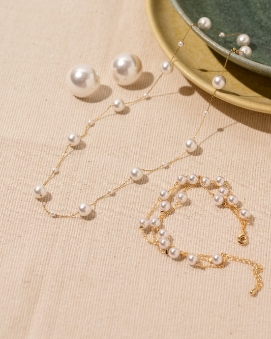 Pearl necklace and bracelet set on a beige surface with a green dish in the background